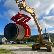 Excavator using pipe lifting clamp device to grip and pick up a concrete pipe.