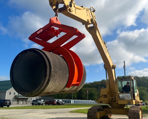 Excavator using pipe lifting clamp device to grip and pick up a concrete pipe.