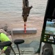 View from cab of mini excavator setting granite stone into water.
