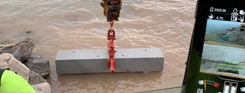 View from cab of mini excavator setting granite stone into water.