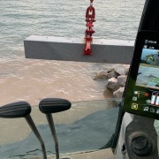 Mini excavator sets a long granite monument into the water for shoreline erosion control.