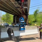 Blue barrier clamp device picking up jersey wall under a bridge.