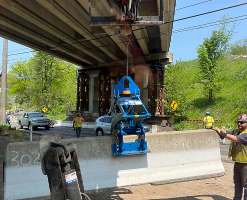 Blue barrier clamp device picking up jersey wall under a bridge.