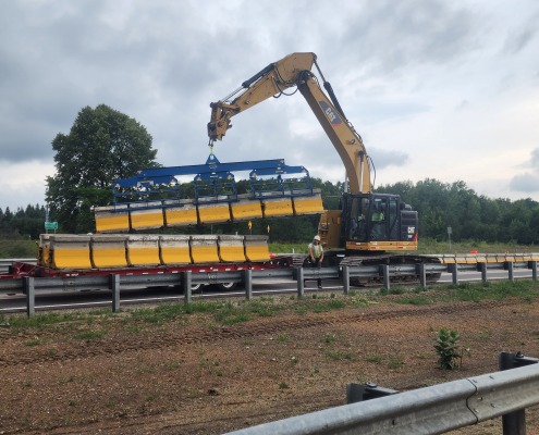 zipper wall segments being picked up by excavator by side of highway