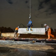 concrete wall barrier on truck bed at night with two construction workers unloading