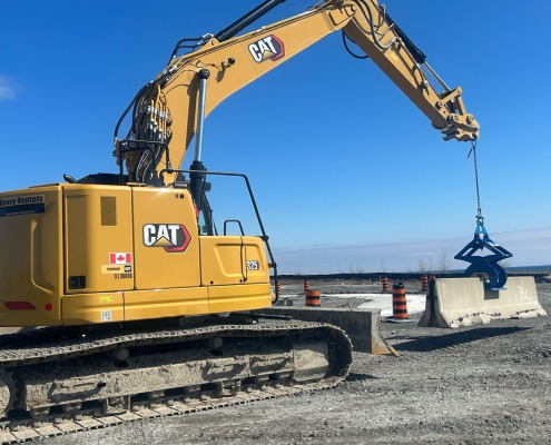 CAT excavator rented from Toromont CAT In Canade picks up a jersey concrete wall with blue Kenco scissor style barrier lift