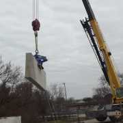 concrete wall with blue scissor clamping device being lifted with a crane