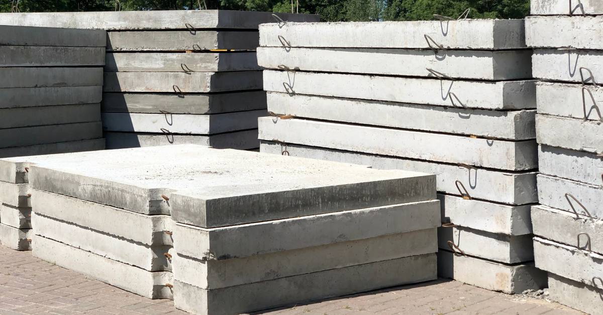 Five groups of stacked, thick slabs of concrete set on top of a brick flooring with hook separators in between each slab.