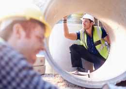 A large concrete pipe. A worker in protective gear is visible through the pipe, inspecting the structure.