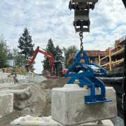 blue scissor lifting clamp picking up large concrete waste block