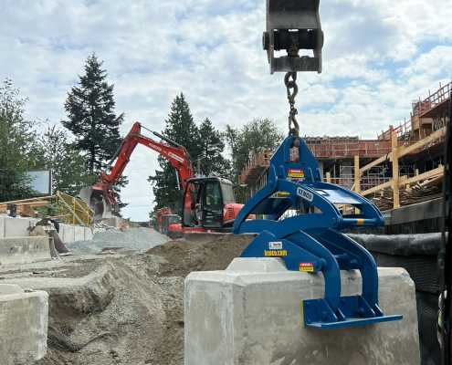 blue scissor lifting clamp picking up large concrete waste block