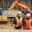 A male and female worker in high visibility gear in front of construction equipment. The man is smiling and holding a clipboard.