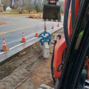 view from inside excavator picking up a concrete curb near side of roadway construction