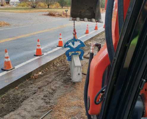 view from inside excavator picking up a concrete curb near side of roadway construction