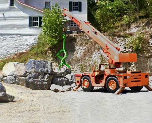 telehandler being used for moving boulders with a green triple tined lifting tool