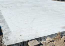 A large, grey concrete slab sits on a muddy construction site full of rubble and other pieces of building debris.