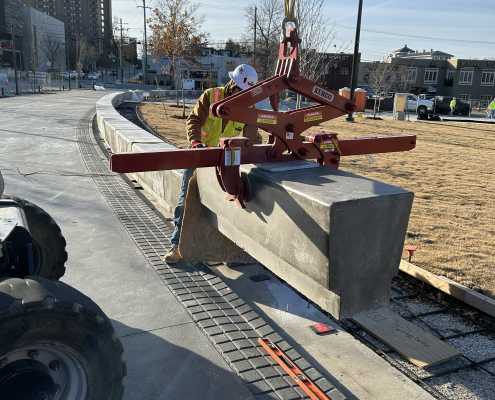 construction worker guiding the installation of concrete precast benches in a row on a jobsite