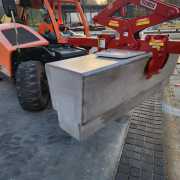 red gripping device hanging from telehandler to lift precast benches