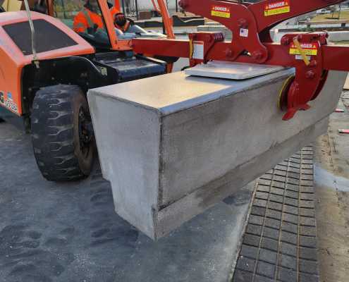 red gripping device hanging from telehandler to lift precast benches