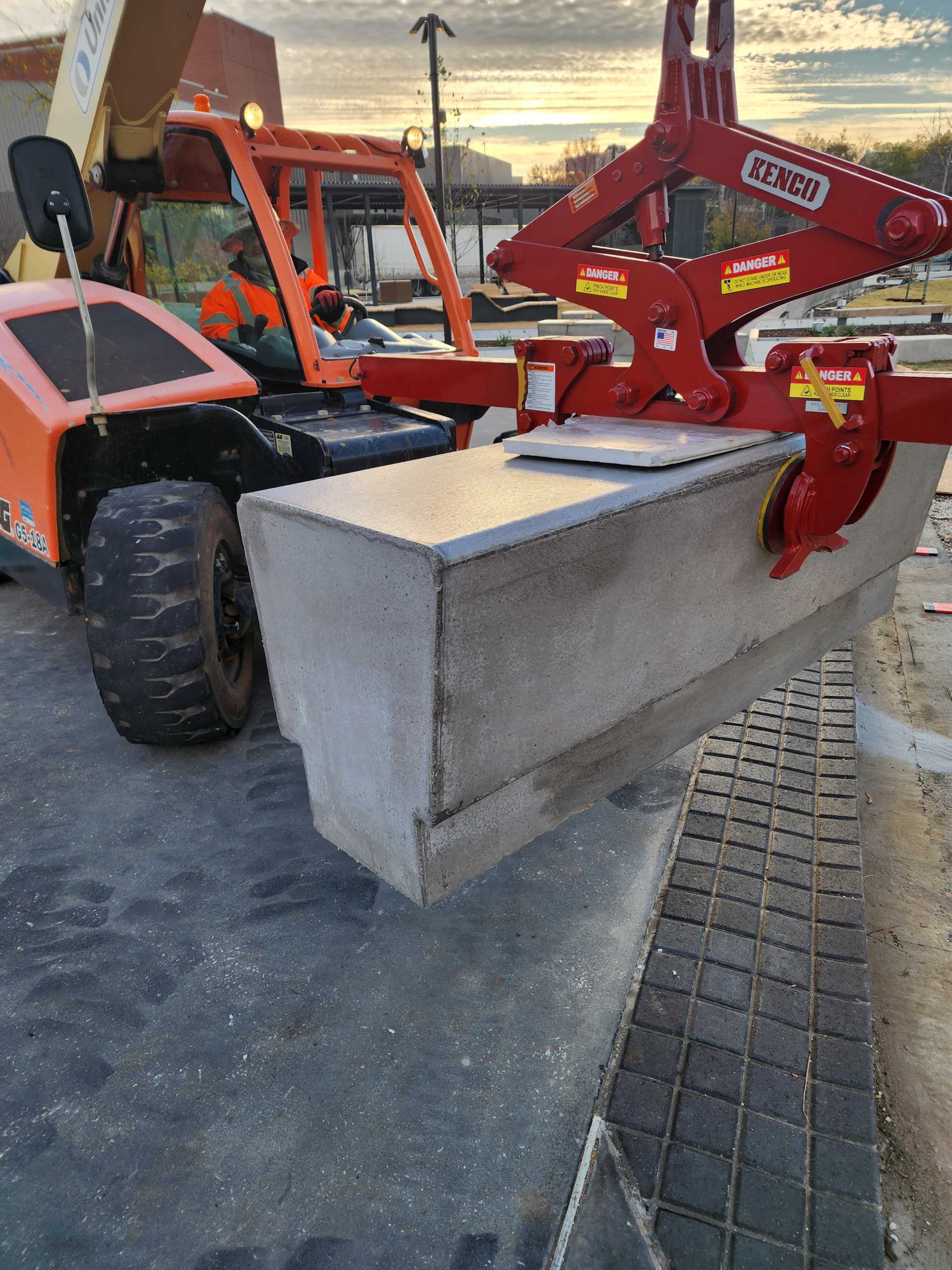 red gripping device hanging from telehandler to lift precast benches