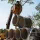 An excavator using a pipe hook to lift concrete pipes from a stack of pipes piled on the back of a large truck.