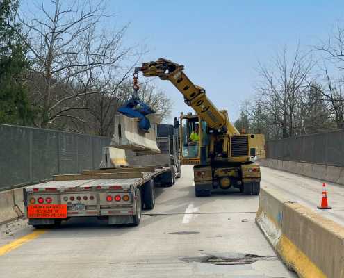 gradall machine setting concrete barrier wall at on bridge and unloading from waiting truck bed