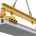 A yellow and black lifting clamp suspended by a chain lifting a precast concrete slab. The clamp is set against a white backdrop.
