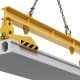 A yellow and black lifting clamp suspended by a chain lifting a precast concrete slab. The clamp is set against a white backdrop.