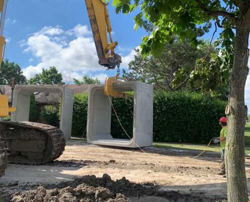 two box culverts side by side sitting on ground with excavator beginning to lift them with lifting hook