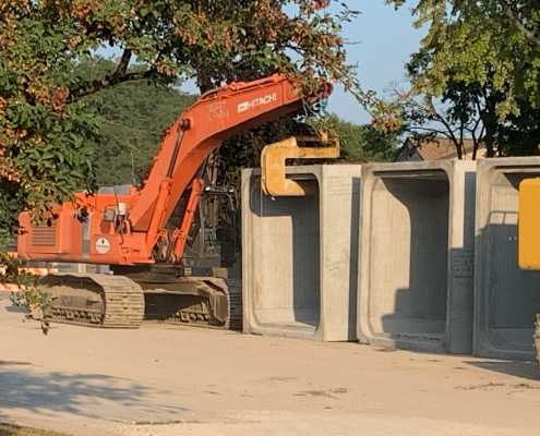 mid size orange excavator prepped to move large box culvert on dirt ground