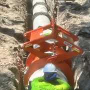 orange pipe lifting device in trench with construction worker with hard hat