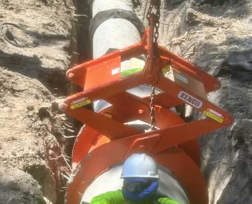 orange pipe lifting device in trench with construction worker with hard hat