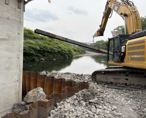 jib boom attachment on machine lifting long piling next to the water