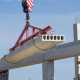 A large slab of concrete is being lifted in the air by lifting attachments. There are concrete columns in the background.