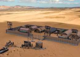 A military compound is sitting alone in the middle of a desert. It is surrounded by barriers. A truck is driving to it.