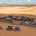 A military compound is sitting alone in the middle of a desert. It is surrounded by barriers. A truck is driving to it.