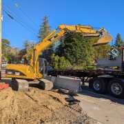 CAT excavator loading precast barriers onto truck using blue scissor clamp at side of roadway with blue sky