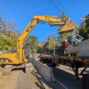 CAT excavator loading precast barriers onto truck using blue scissor clamp in front of blue skies