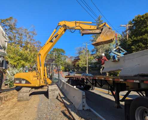 CAT excavator loading precast barriers onto truck using blue scissor clamp in front of blue skies