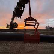 silhouette of excavator lifting a pipe with a kenco pipe lift with sun setting and silhouette of a man standing on the track