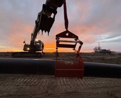 silhouette of excavator lifting a pipe with a kenco pipe lift with sun setting and silhouette of a man standing on the track