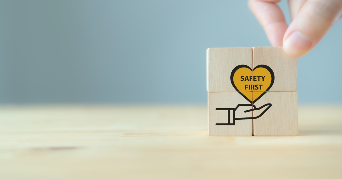 A hand places wooden blocks with a safety-first icon and heart symbol on a table, representing workplace safety.