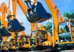 A row of yellow excavators with raised buckets lined up at a construction equipment yard, ready for jobsite work.