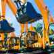 A row of yellow excavators with raised buckets lined up at a construction equipment yard, ready for jobsite work.