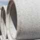 Stacked precast concrete pipes are aligned on a construction site, showing smooth cylindrical surfaces.