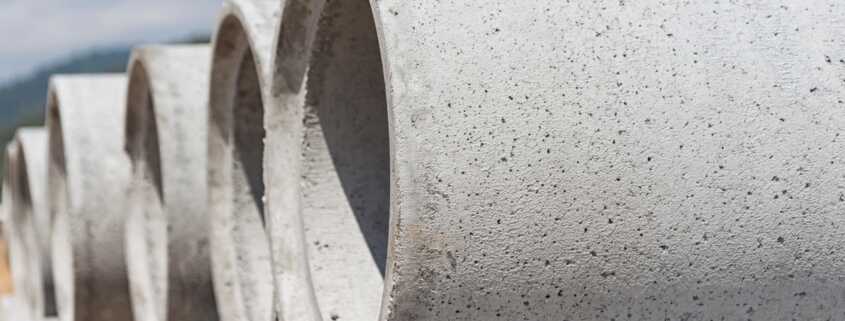 Stacked precast concrete pipes are aligned on a construction site, showing smooth cylindrical surfaces.